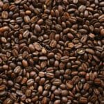 Dark roasted coffee beans on a black surface, a common cause of bitter-tasting coffee