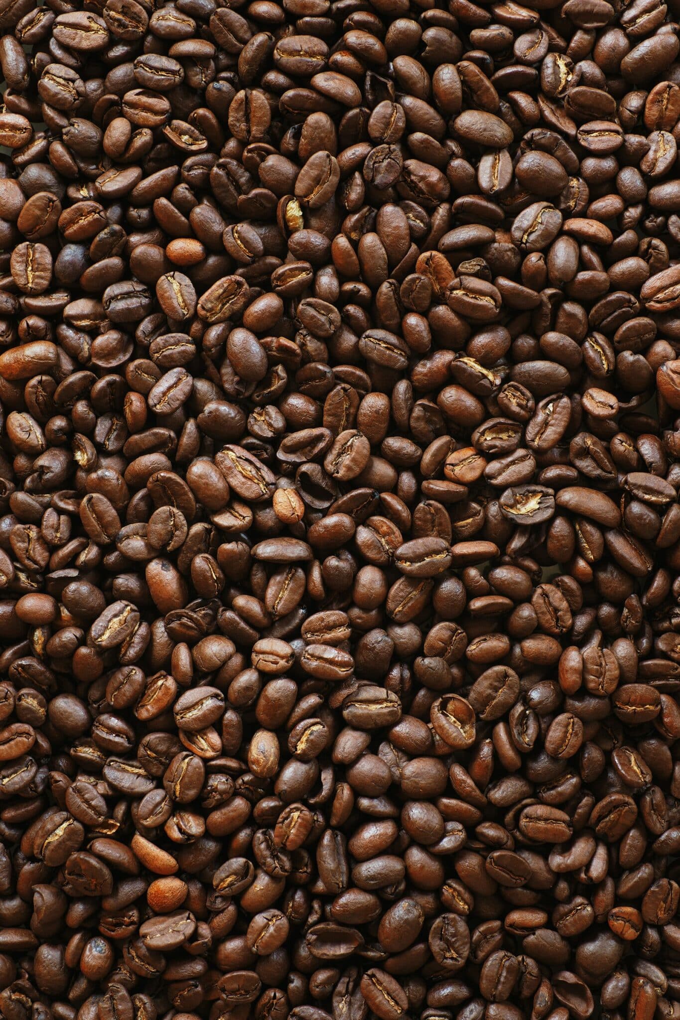 Dark roasted coffee beans on a black surface, a common cause of bitter-tasting coffee